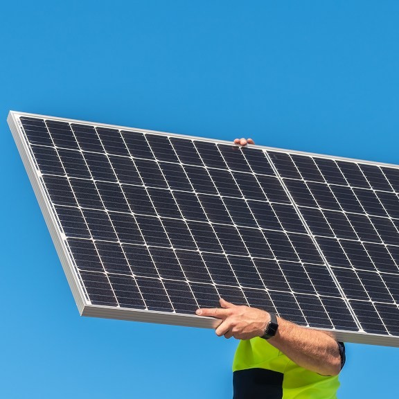 Australian electrician carrying a solar panel outside.