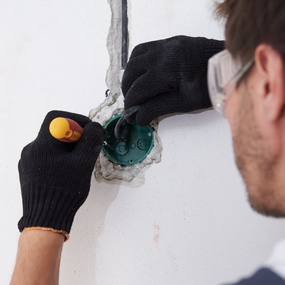 Electrician with safety glasses and rubber gloves instaling a wall socket.