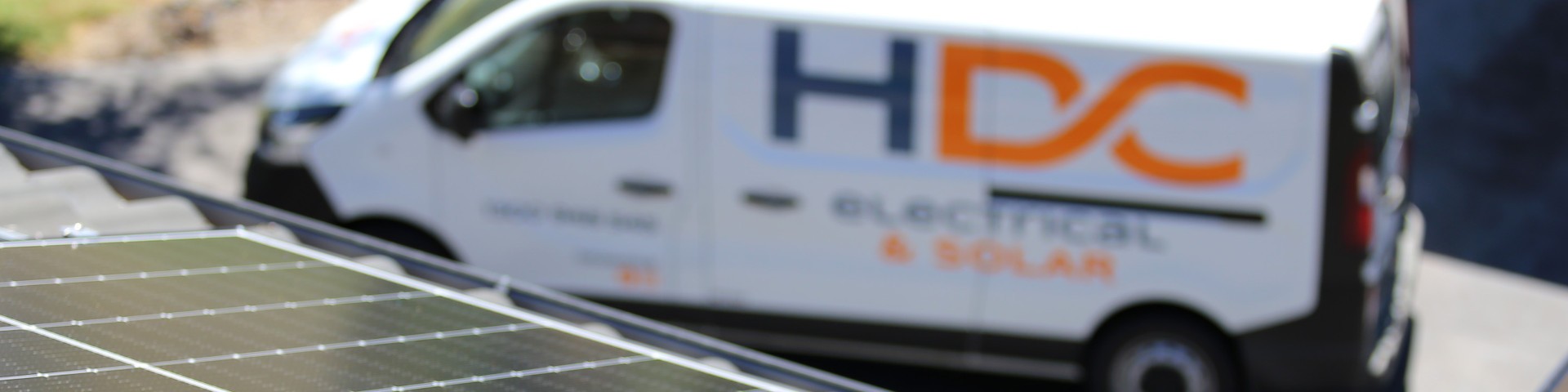 HDC Electrical and Solar van parked near a roof with solar panels.