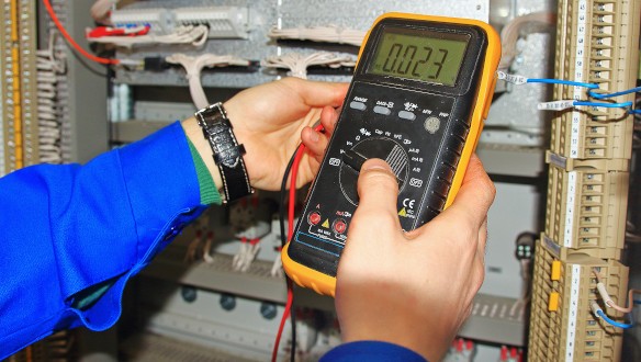 Electrician performing industrial electrical work with a multimeter.